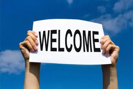 Hands holding welcome sign against sky