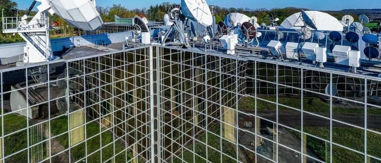 Mirrored glass building reflecting rooftop satellite dishes