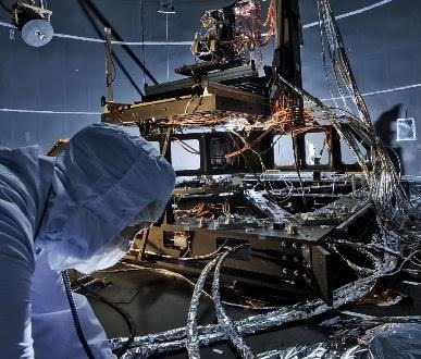 Technician in clean suit inspecting complex scientific instrument